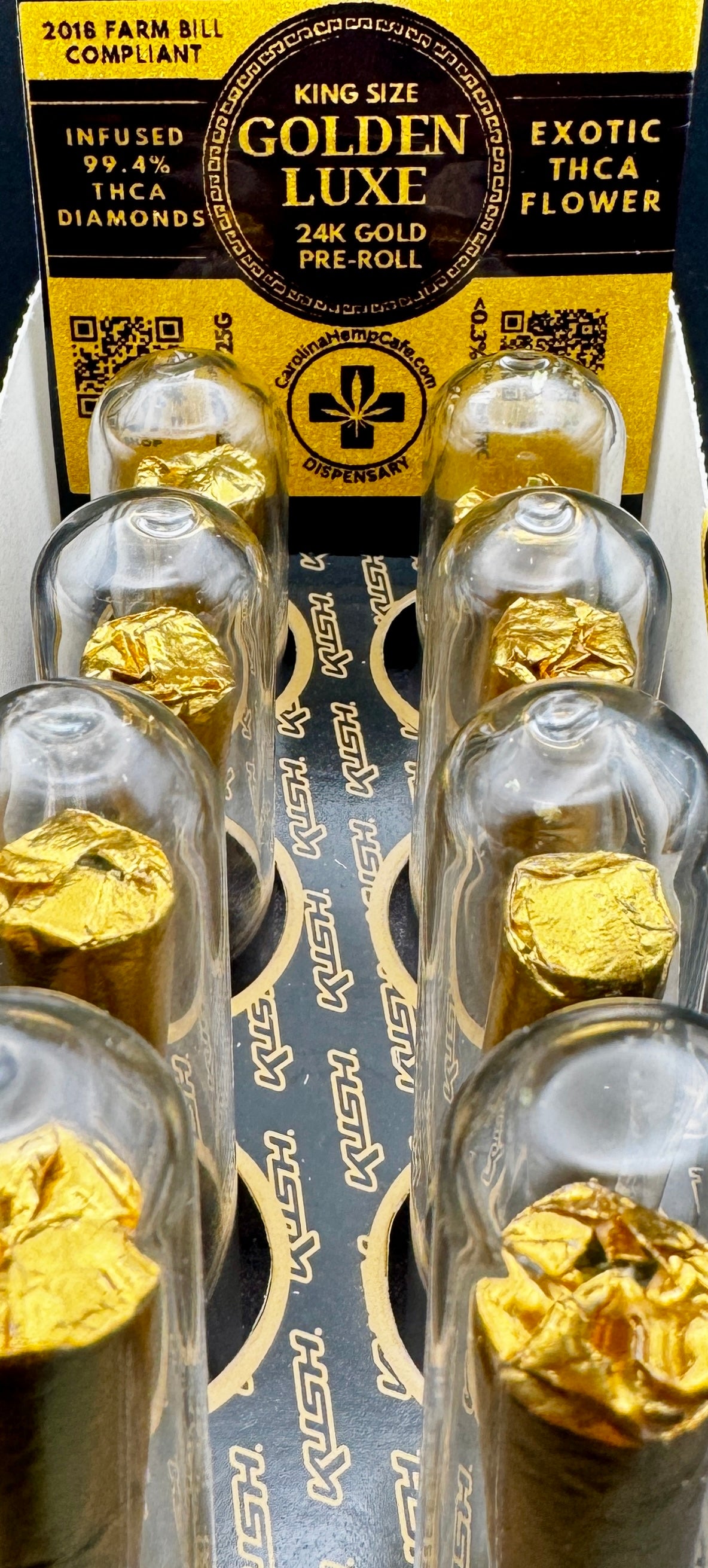 Gold pre-rolls in a clear tubes with a yellow label on a white background. Display box with 8 of them