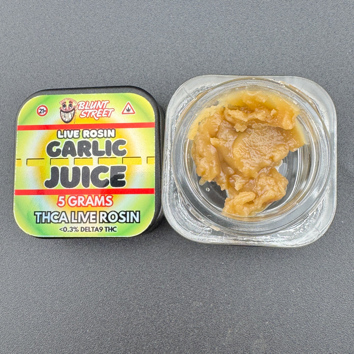 Container of garlic juice rosin with a colorful label on a gray background