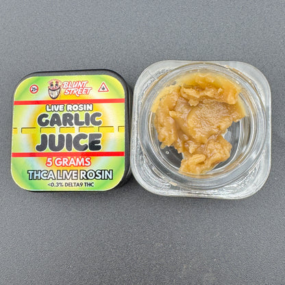 Container of garlic juice rosin with a colorful label on a gray background