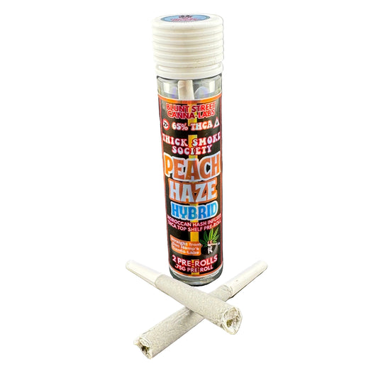 A clear plastic bottle of Peach Haze Hybrid pre-rolled joints with a white screw cap, standing upright on a dark gray surface, with two rolled joints placed in front of it.