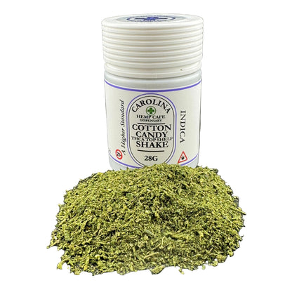 A white plastic jar labeled Carolina Hemp Cafe Hempindies Cotton Candy THC Top Shelf Shake 28G, shown with a pile of dried green herbal tea blend in front on a white background.