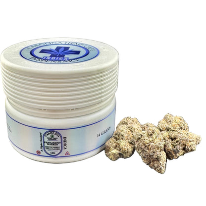 A white plastic jar of Cannabina Healths Indica H Grains next to several dried cannabis buds on a gray textured background.