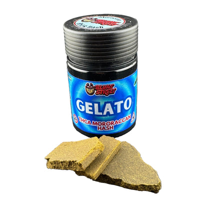 A jar of Slush Street Gelato Incamoroccan Hash next to two broken pieces of the golden-brown hash butter on a dark gray background.