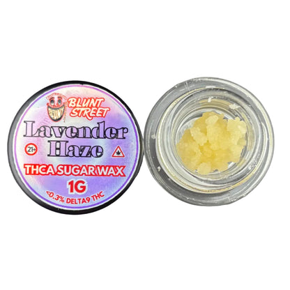 An open jar of Blunt Street Lavender Haze THCA sugar wax next to its purple and red branded lid, showing the pale yellow wax crystals inside a clear container on a dark gray background.