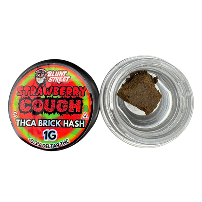 A round clear plastic jar of Blunt Street Strawberry Cough THCA brick hash with its colorful red, green, and black label visible, shown next to an open jar containing a brown hash piece on a white background.