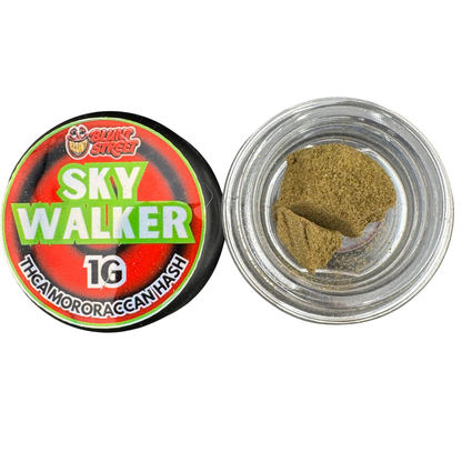 A round jar of Skyy Walker 1G THCA gummy or roachant hash shown open with its lid beside it. The lid features a red, black, and green label with the brand name 'Bluntz Bros.